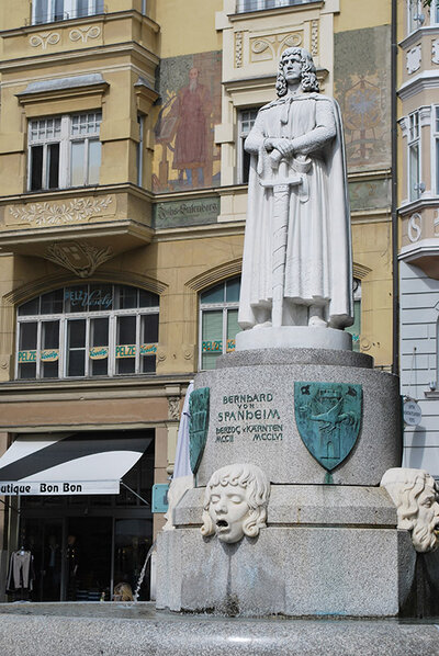 Das Denkmal des Stadtgründers Bernhard von Spanheim vor der Fassade des reich mit Fresken und Stuck verzierten Hauses am Arthur-Lemisch-Platz