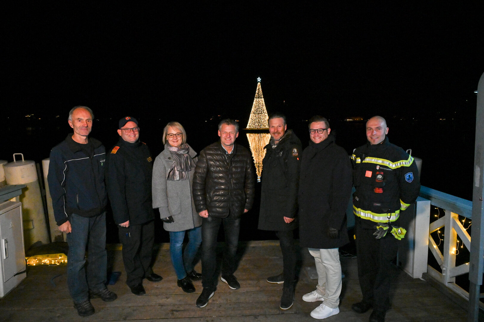 Bürgermeister Christian Scheider freut sich gemeinsam mit Stadtgartenreferent Stadtrat Julian Geier, Branddirektor DI Herbert Schifferl, Branddirektor-Stellvertreter Wolfgang Germ, Mag. Elisabeth Kos (Abt. Stadtgarten) und den Mitarbeitern der Abteilung Stadtgarten sowie der Berufsfeuerwehr Klagenfurt über die Aufstellung des schwimmenden Christbaumes in der Wörthersee Ostbucht. Foto: StadtKommunikation/Hronek