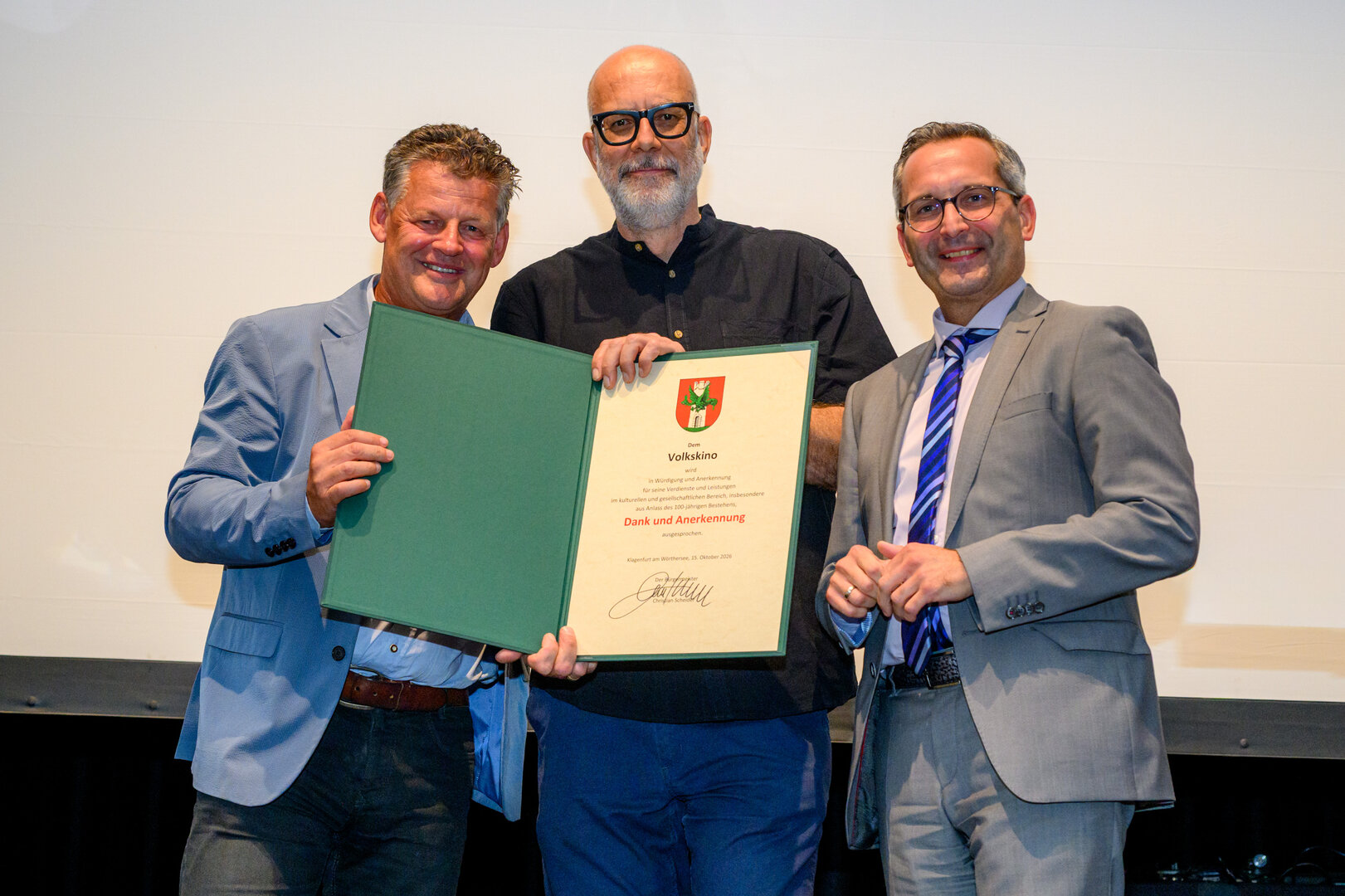 Bürgermeister Christian Scheider und Kulturreferent Stadtrat Mag. Franz Petritz überreichten dem Obmann des Vereins „Neues Volkskino“, Robert Schabus, die Dank- und Anerkennungsurkunde seitens der Landeshauptstadt Klagenfurt. Foto: StadtKommunikation/Hude